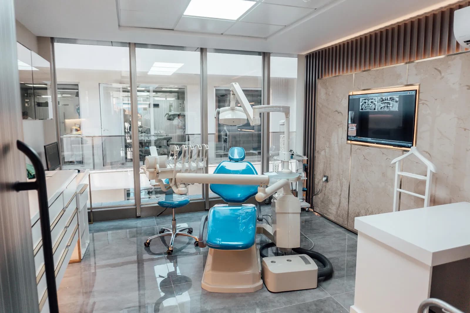A treatment room at Ballıpınar Dental with a dental chair, overhead light and a screen showing panoramic dental X-rays