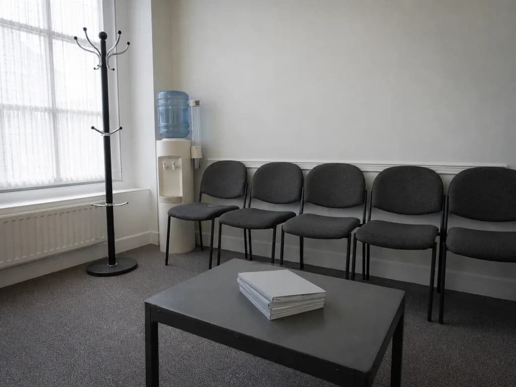 An empty UK waiting room with upholstered chairs and grey daylight through a window