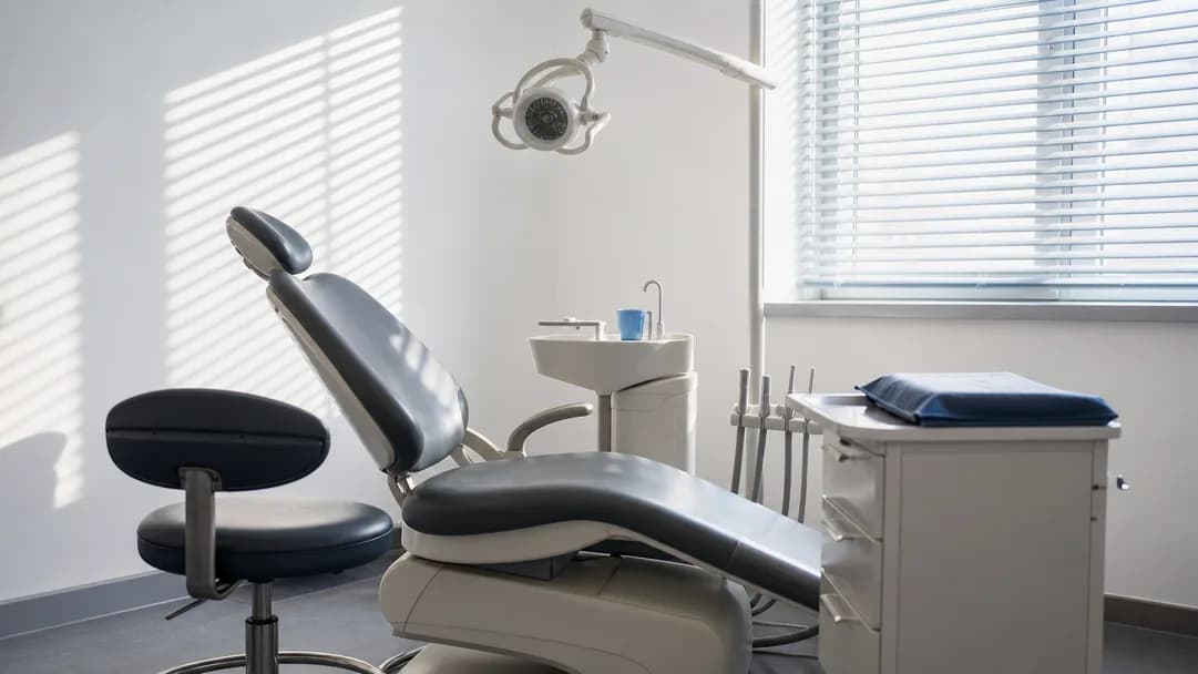 An empty UK treatment room with a dentist's stool and daylight through a blind