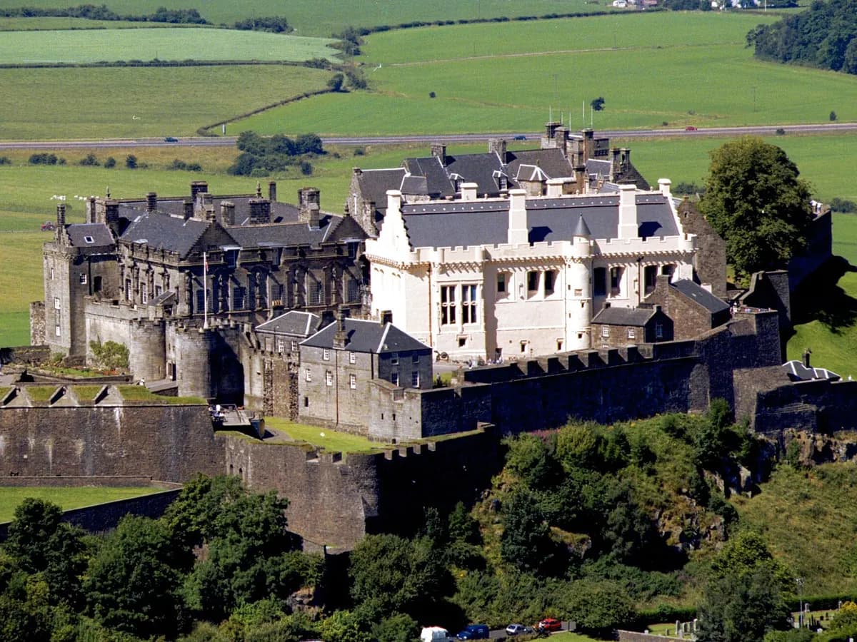 Stirling: a castle on a sheer crag with a tall Gothic monument tower on a wooded hill opposite