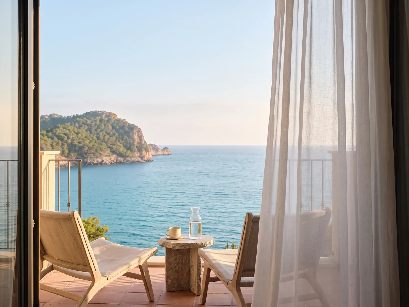 The balcony of the same hotel room, two low chairs and a stone table facing the sea
