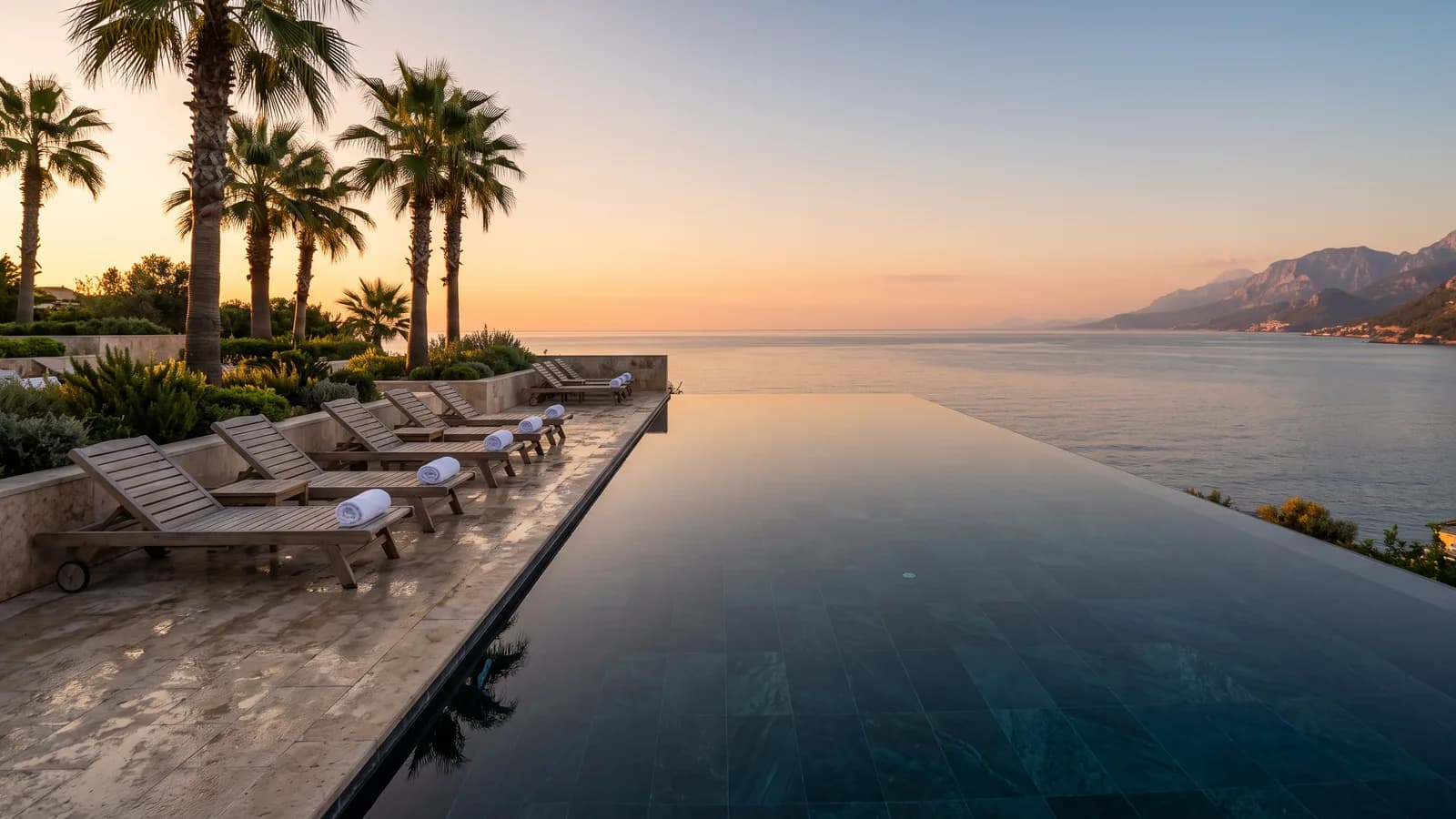 A hotel pool terrace at golden hour, empty loungers under palms with the Mediterranean beyond
