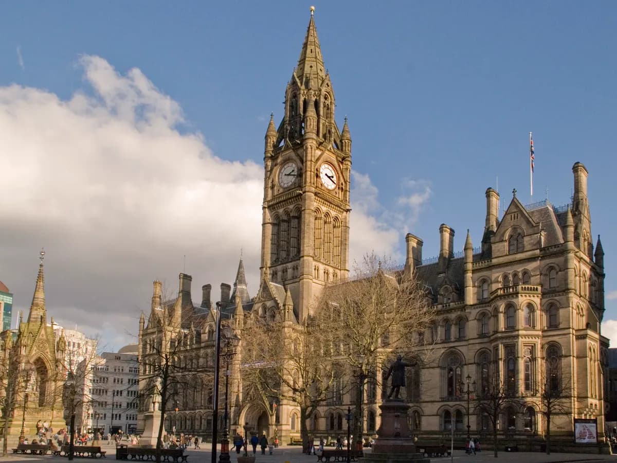 Manchester: red-brick Victorian warehouses along a canal with a tram and a tall glass tower behind